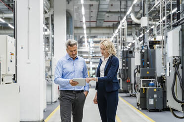 Businesswoman explaining colleague over tablet PC in factory - DIGF17110