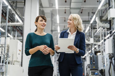 Lächelnde Geschäftsfrauen, die in einer modernen Fabrik diskutieren - DIGF17114