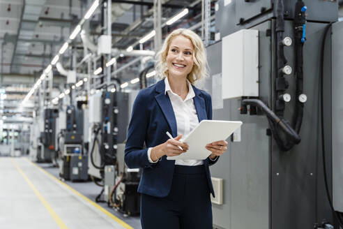 Smiling businesswoman with tablet PC at industrial equipment - DIGF17122