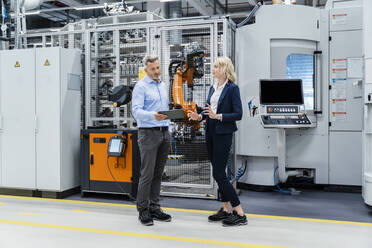 Businesswoman discussing with coworker holding tablet PC in factory - DIGF17143