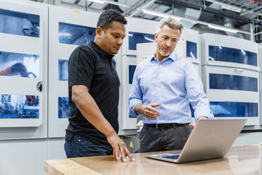 Businessman discussing over laptop with coworker in factory - DIGF17157