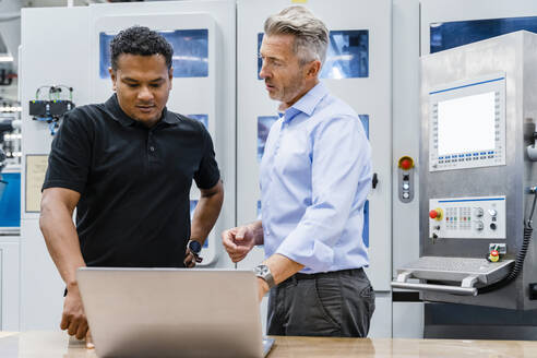 Geschäftsmann mit Laptop und Ingenieur am Schreibtisch in einer Fabrik - DIGF17158