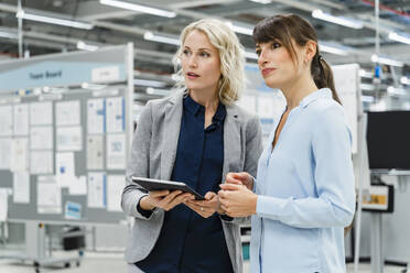 Businesswoman holding tablet PC with coworker at factory - DIGF17176