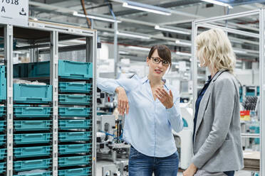 Businesswoman discussing with colleague by rack in factory - DIGF17181