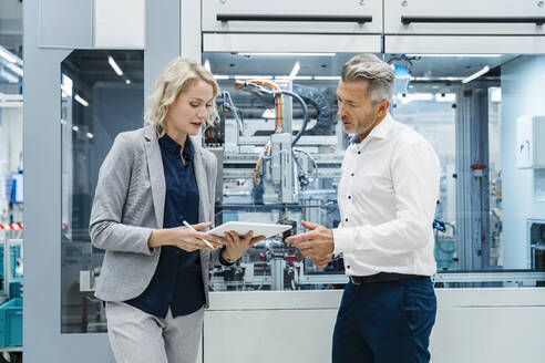 Geschäftsfrau diskutiert mit einem Kollegen über einen Tablet-PC in einer modernen Fabrik - DIGF17183