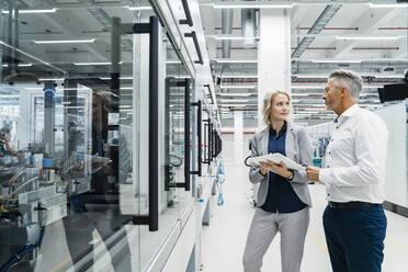 Businesswoman discussing with coworker at industrial machinery - DIGF17190