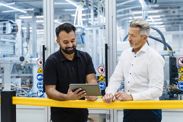 Businessmen using tablet PC at railing in factory - DIGF17231