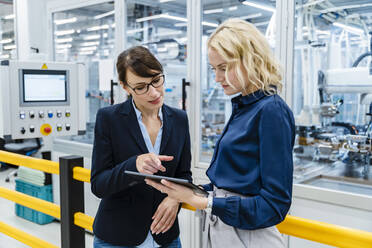 Geschäftsfrau diskutiert mit einem Kollegen über einen Tablet-PC in einer Fabrik - DIGF17240