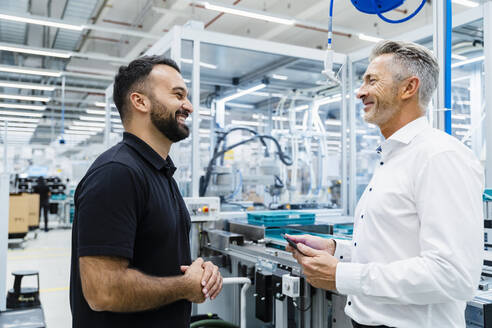 Smiling engineer discussing with businessman at automated industry - DIGF17245