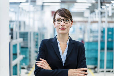 Confident businesswoman with arms crossed at factory - DIGF17301