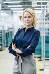 Confident businesswoman with arms crossed at automated factory - DIGF17307