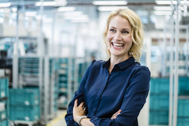 Happy businesswoman with arms crossed at industry - DIGF17308