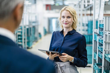 Geschäftsfrau mit Tablet-PC blickt auf einen Kollegen in der Industrie - DIGF17310