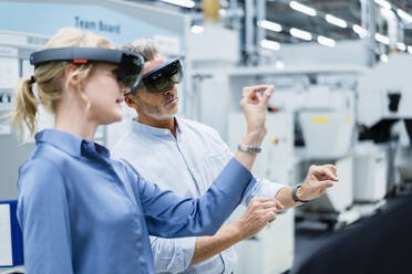 Coworkers discussing and using augmented reality eyeglasses in factory - DIGF17334