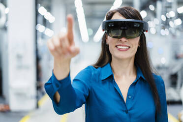 Smiling businesswoman using augmented reality eyeglasses at industry - DIGF17338