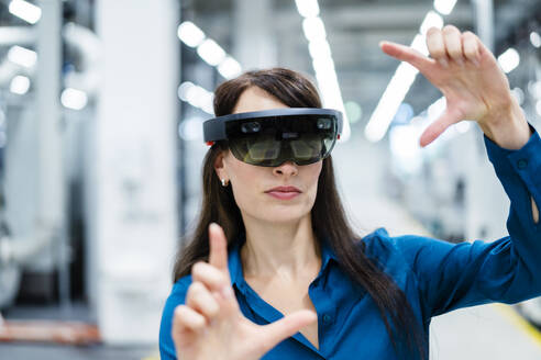 Geschäftsfrau mit Augmented-Reality-Brille macht Fingerrahmen in der Industrie - DIGF17339