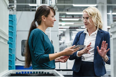 Businesswoman discussing with colleague holding tablet PC In industry - DIGF17350