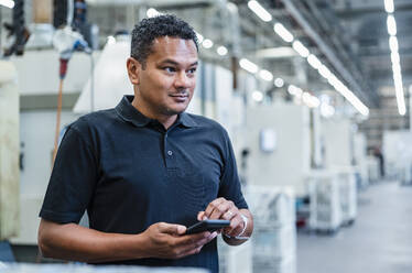 Engineer holding smart phone at automated factory - DIGF17352