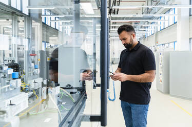 Ingenieur mit Mobiltelefon an einer Industriemaschine hinter Glas - DIGF17364