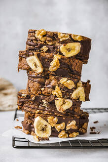 Sliced banana cake with walnuts and chocolate sauce stacked on cooling rack - FLMF00769