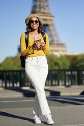 Glücklicher Tourist mit Smartphone vor dem Eiffelturm, Paris, Frankreich - KIJF04359