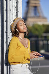 Woman with eyes closed listening music leaning on metal column, Paris, France - KIJF04366