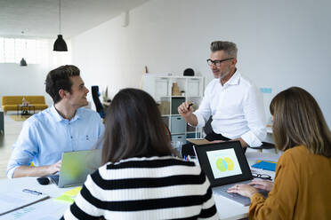 Businessman sitting on desk discussing with team working at office - GIOF14496