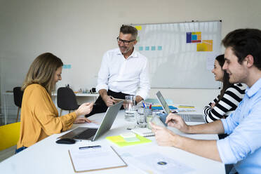 Smiling businessman and colleagues sitting on desk at office - GIOF14497