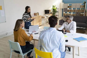 Junge Geschäftsfrau diskutiert mit Kollegen am Schreibtisch sitzend im Büro - GIOF14507