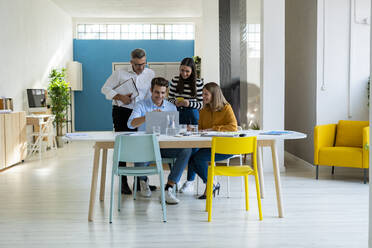 Young businessman with laptop sitting at desk with colleagues in office - GIOF14512