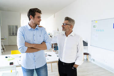 Businessman with hand in pocket talking to colleague standing at office - GIOF14535