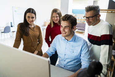 Kollegen schauen sich gemeinsam einen Desktop-PC im Coworking-Büro an - GIOF14541