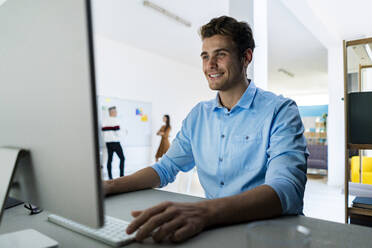 Lächelnder Geschäftsmann bei der Arbeit an einem Desktop-PC im Büro - GIOF14544