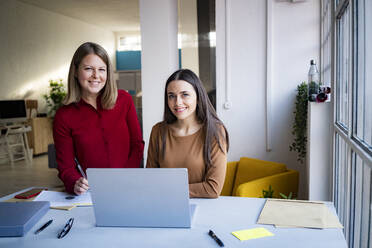 Lächelnde Geschäftsfrauen mit Laptop am Schreibtisch im Büro - GIOF14552