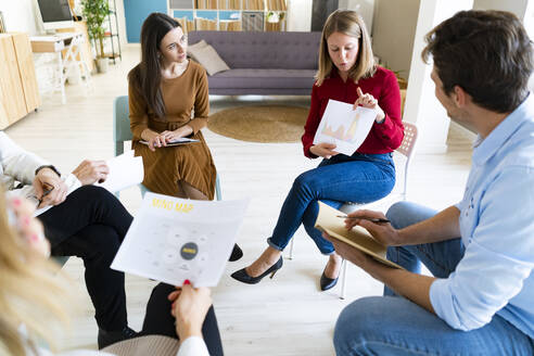 Businesswoman explaining reports to colleagues in office meeting - GIOF14566