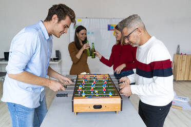 Businessman with colleague playing foosball in office - GIOF14584
