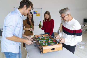 Playful colleagues playing foosball with coworkers drinking beer in office - GIOF14585