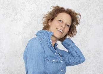 Woman with head in hair wearing denim shirt at home - JBYF00072