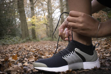 Close up female runner tying shoelace in autumn woods - CAIF31810