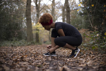 Young female runner tying shoelace in autumn woods - CAIF31816