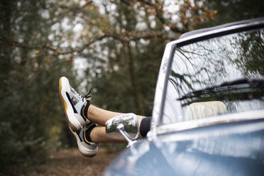 Unbekümmerte junge Frau entspannt sich in einem Cabrio mit den Füßen im Fenster - CAIF31819