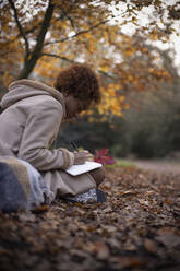 Junge Frau, die im Herbstlaub Tagebuch führt - CAIF31821