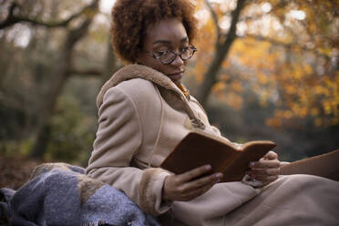 Serene young woman reading in autumn park - CAIF31822