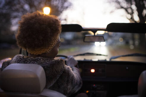 Young woman driving convertible on road at dusk - CAIF31856