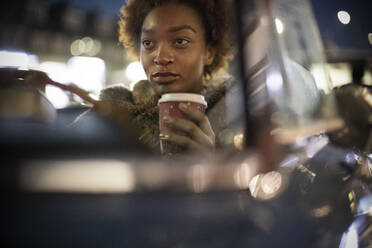 Junge Frau mit Kaffee am Steuer eines Cabriolets bei Nacht - CAIF31859