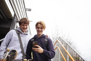 Glückliche Teenager, die auf der Treppe ein Smartphone benutzen - CAIF31871