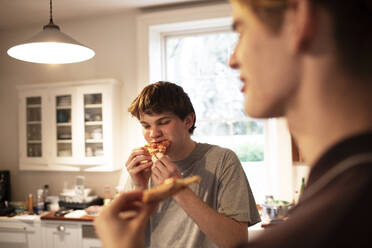 Teenage boys eating pizza in kitchen - CAIF31873