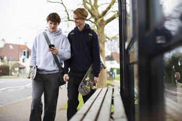 Teenager mit Skateboard und Smartphone an der Bushaltestelle - CAIF31882