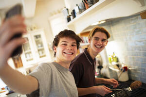Glückliche Teenager-Jungen nehmen Selfie und Kochen in der Küche - CAIF31883