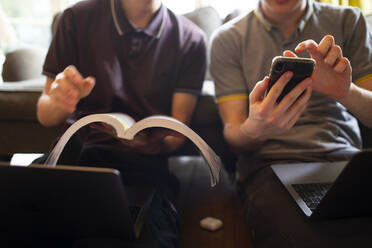Teenager mit Lehrbuch und Smartphone beim Lernen zu Hause - CAIF31887